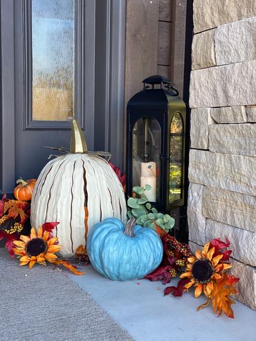Fall-themed porch decor with pumpkins, sunflowers, and a lantern.