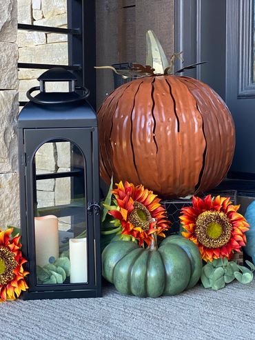 Seasonal fall decoration with pumpkins, sunflowers, and a lantern by a door.