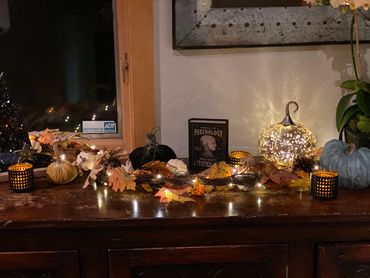 Cozy autumn display with pumpkins, fairy lights, and candles on a wooden surface.