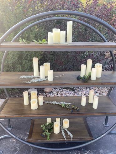 Decorative LED candles and foliage arranged on circular wooden shelves outdoors.