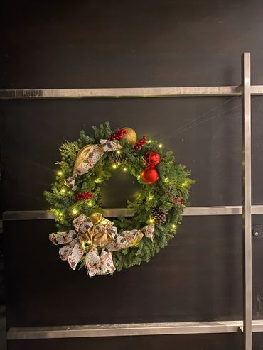 Festive Christmas wreath adorned with lights, ornaments, and ribbons on a dark door.