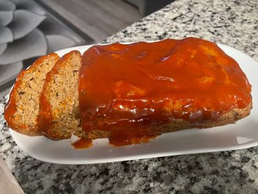 Meatloaf topped with rich tomato sauce on a white plate.