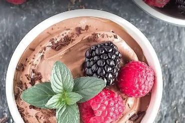 Chocolate mousse topped with fresh berries and mint leaves in a white bowl.
