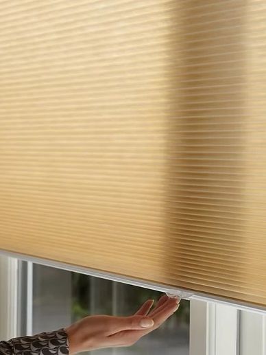 Hand adjusting a beige cellular window blind.