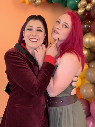 Two women smiling and posing closely in front of colorful balloons.