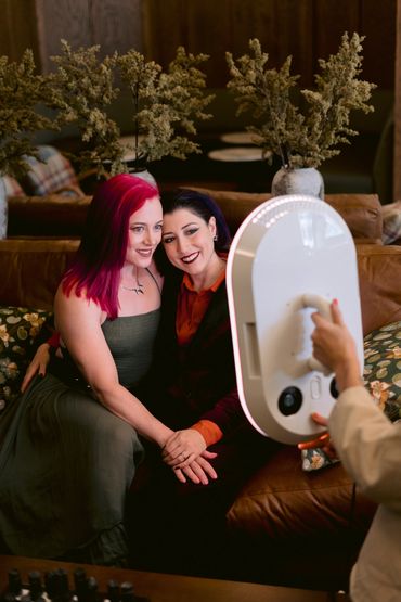 Two women smiling and posing for a photo with a ring light on a couch.