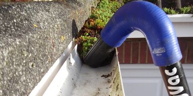 A blue and black Ryvac tool cleaning debris from a white gutter.