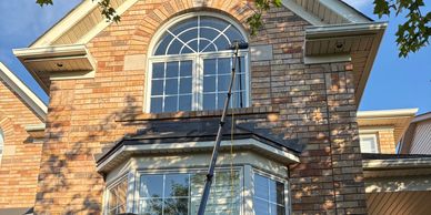 A person cleaning a high window with a long pole outside a brick house.