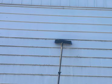A cleaning brush on a long pole against a dirty white siding wall.