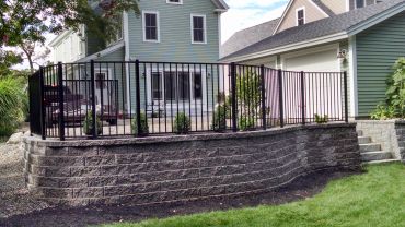 A stone retaining wall with a black metal fence surrounding a raised garden area.