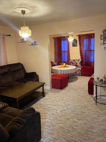 Cozy living room with brown sofas and a charming adjacent dining area with red curtains.