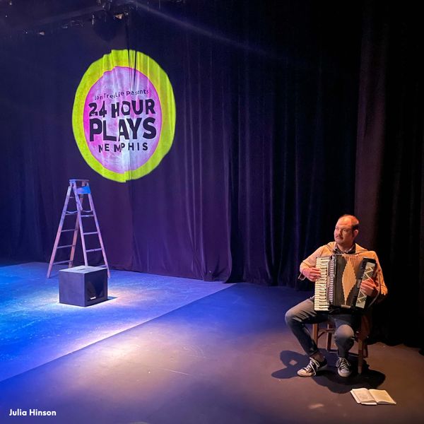 Man plays accordion on theatrical stage.