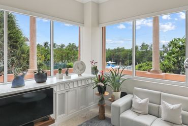 Bright living room with large windows, green plants, and white sofa overlooking a garden and water view.