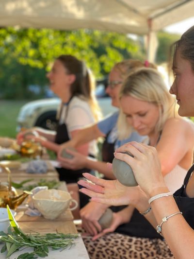 Group of women crafting pottery outdoors on a sunny day.