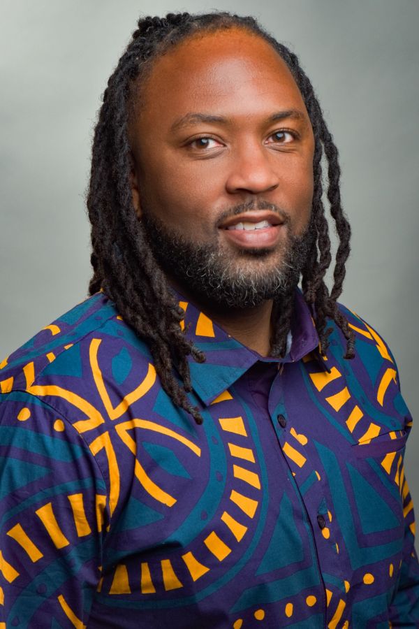 Man with dreadlocks wearing a colorful patterned shirt.