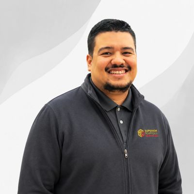 Smiling man in a black jacket with a company logo on a light background.
