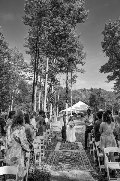 Bride and groom walking down outdoor aisle surrounded by guests.