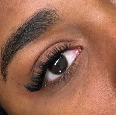 Close-up of a brown eye with long, curled eyelashes and a well-groomed eyebrow.