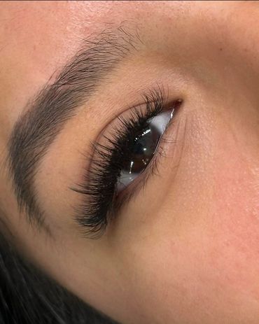 Close-up of a brown eye with long, thick eyelashes and a well-groomed eyebrow.
