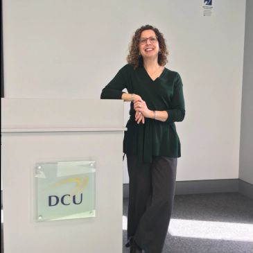 Woman smiling and leaning on a podium with DCU logo.