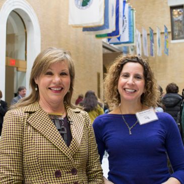 Two women smiling at an indoor event.