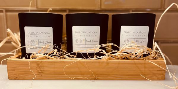 Three black Quentin Latham candles in a wooden tray with straw.