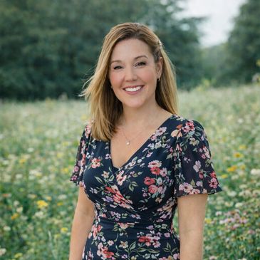 Smiling woman in floral dress standing in a wildflower field.