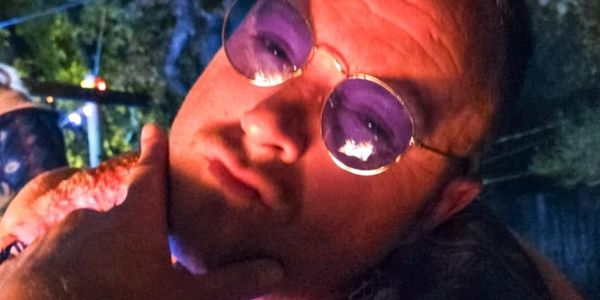 Man wearing reflective round glasses in a low-lit outdoor setting.