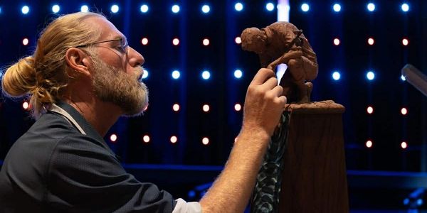 Artist sculpting a detailed figure under dramatic lighting.