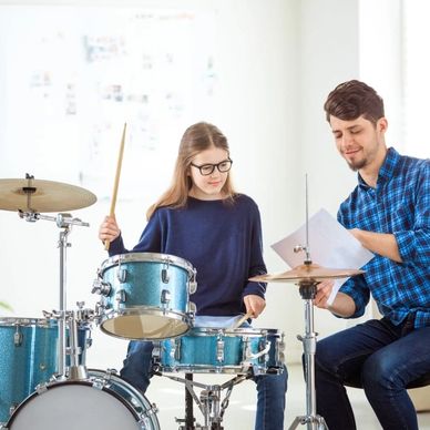 Drum instructor showing music to a young girl playing drums