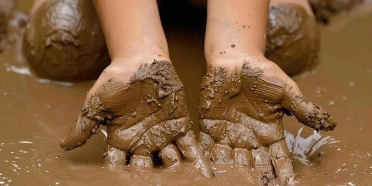 Hands covered in thick, wet mud with muddy knees in the background.