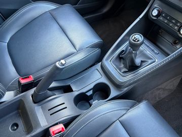 Interior of a car showing leather seats, manual gear shift, and cup holders.