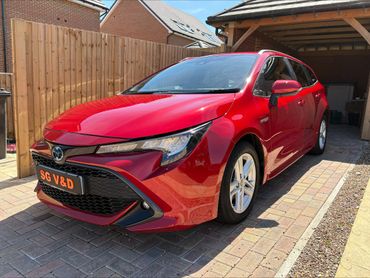Red Toyota hybrid car parked in a driveway beside a wooden fence.