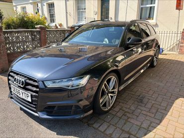 Shiny black Audi car parked on a driveway under sunlight.