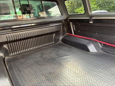 Empty black truck bed with a red strap and rubber mat.