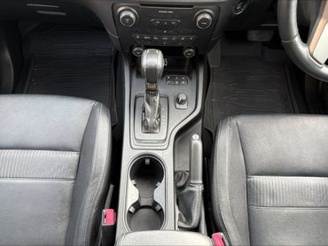 Car interior center console with gear shift and cup holders.
