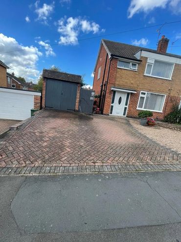 A brick driveway leading to a garage beside a brick house on a clear day.