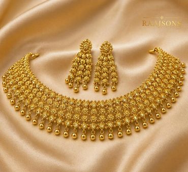 Intricate gold necklace and matching earrings set on satin fabric.