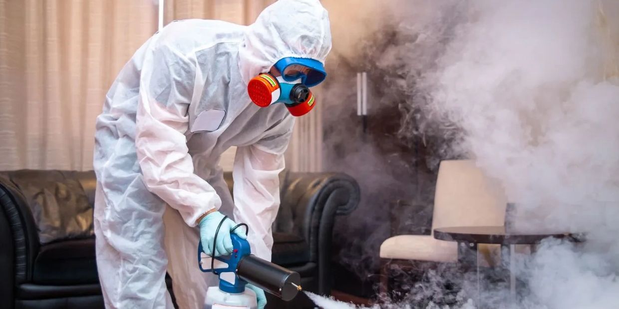 Person in protective gear fumigating a room indoors.