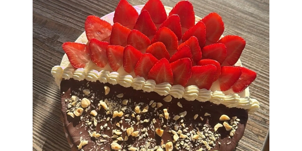 Chocolate cake topped with fresh strawberries, cream, and chopped nuts on a wooden table.