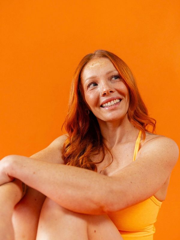 Smiling red-haired woman in orange top against orange background.