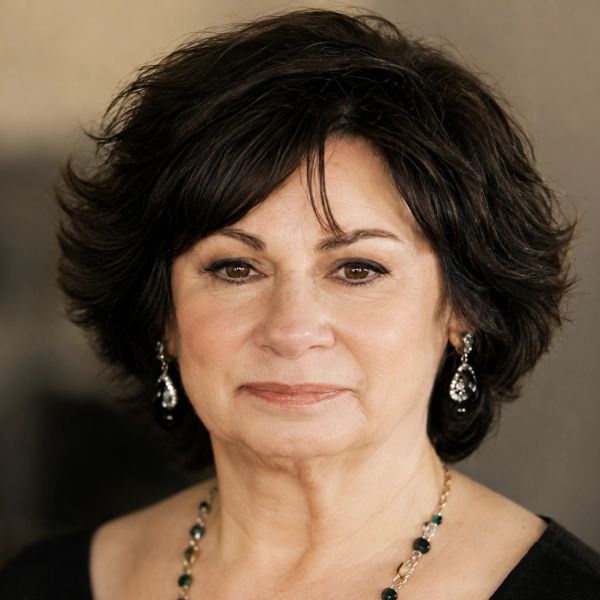 Portrait of a mature woman with dark hair and elegant jewelry.
