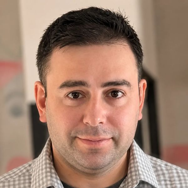 Man with short dark hair wearing a checkered shirt, looking at the camera.