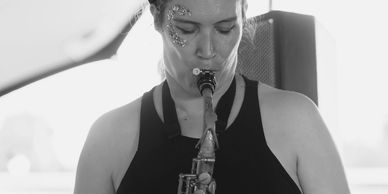 Dark haired lady with blue glitter on the side of her face playing the saxophone.