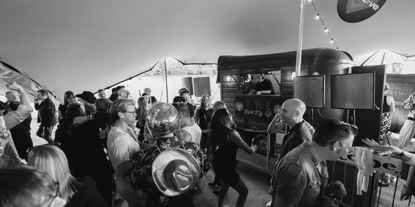 Group of people dancing and having fun in front of a DJ playing music from a horse box in a teepee.