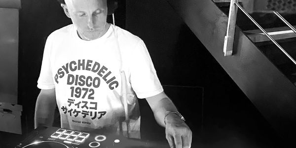 Image of a person wearing headphones and DJing on a controller illuminated with blue lights.