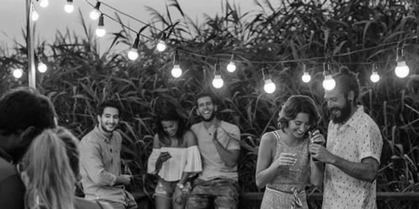 Group of people drinking, eating and laughing outside under festoon lights.