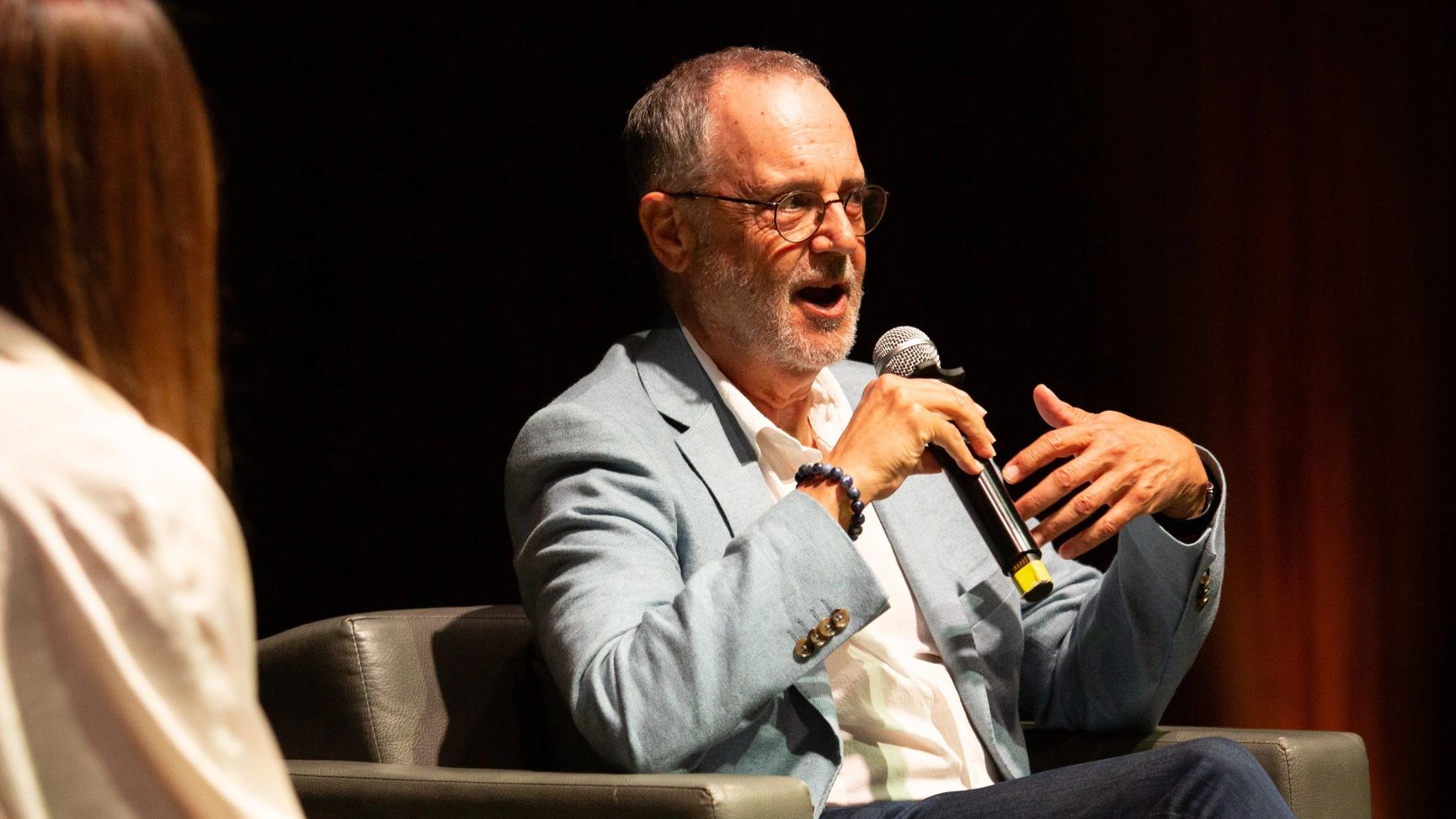 Elderly man with glasses speaking into microphone during an event.