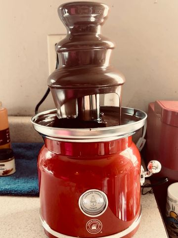 A red chocolate fountain flowing with melted chocolate on a kitchen counter.