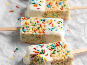 Rice Krispies treats dipped in white chocolate with sprinkles on sticks.